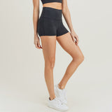 The bottom half of a woman posing to the side against a white background wearing the black shorts and white sneakers.