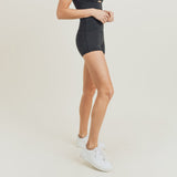 The bottom half of a woman posing to the side against a white background wearing the black shorts and white sneakers.