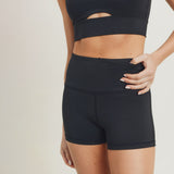 The torso of a woman posing against a white background wearing the black shorts with her hand on her hip and thumb in the waistline hidden pocket.