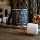 Folklore candle in a tin with marshmallows and kindling on a wood surface