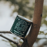 Candle labeled 'In the Pines' balancing on a tree branch