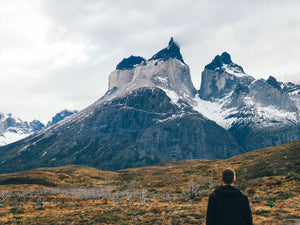 A man faces snowcapped peaks on a cloudy day in Chile.