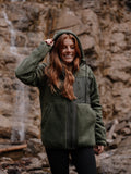 Girl wearing a green hooded jacket standing in front of a rocky background