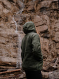 Girl wearing a green hooded jacket standing in front of a rocky background