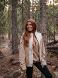 Woman standing in a forest wearing a vest over a long sleeve shirt.