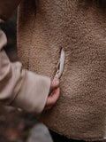 Close-up of of the fuzzy vest fabric with a hand holding the zipper of the hand pocket