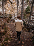 Woman walking away from the camera in a canyon wearing a vest over a long sleeve shirt.