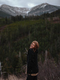 Woman wearing a black jacket standing in a field with mountains in the background