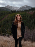 Woman wearing a black jacket standing in a field with mountains in the background