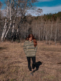 Woman wearing a patterned fleece walking in a field with trees in the background