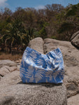 The tote sits on a rock on the beach with palms in the background.