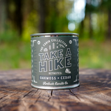 Take a Hike candle tin sitting on a smooth wood surface in the forest
