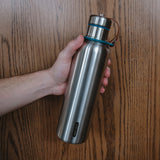 The hand of a man holding the water bottle in front of a wood background.