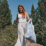 A girl carries the tote through a wooded area. The tote is extended towards the camera.