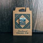 The pin attached to its packaging, which is a cardboard tag. The pin design features rugged mountains with the words 'Rocky Mountains' at the bottom.