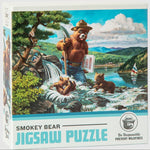 The front of the puzzle box reading 'Smokey Bear Jigsaw Puzzle' and showing the puzzle image, which is Smokey holding a shovel and a book that says 'Prevent Forest Fires.' He is standing by a waterfall and lake surrounded by mountains where two bear cubs play in the cascade.